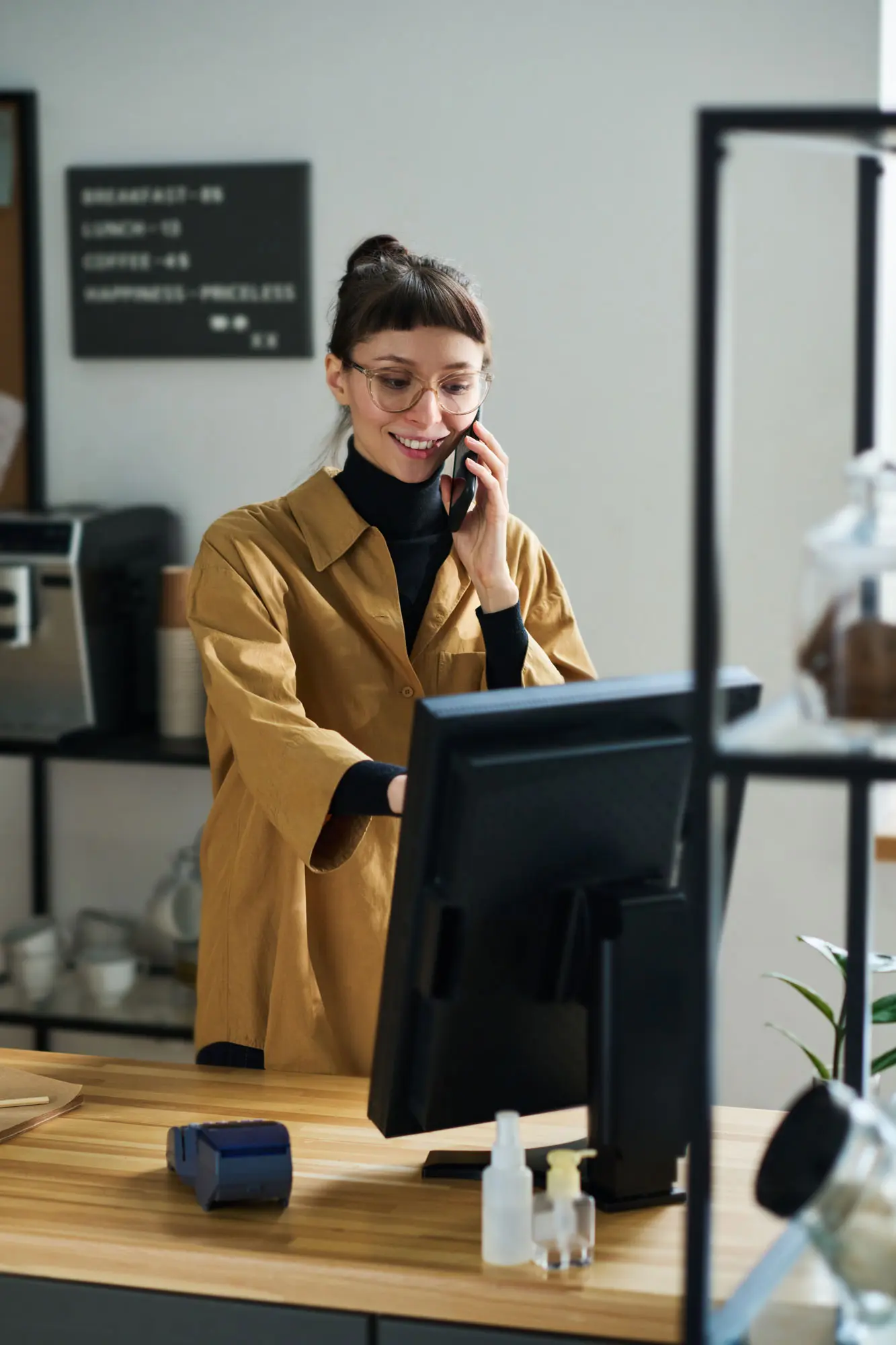 Lächelnde Frau bespricht Display-Werbung am Telefon, während sie einen Computer in einem Café benutzt.