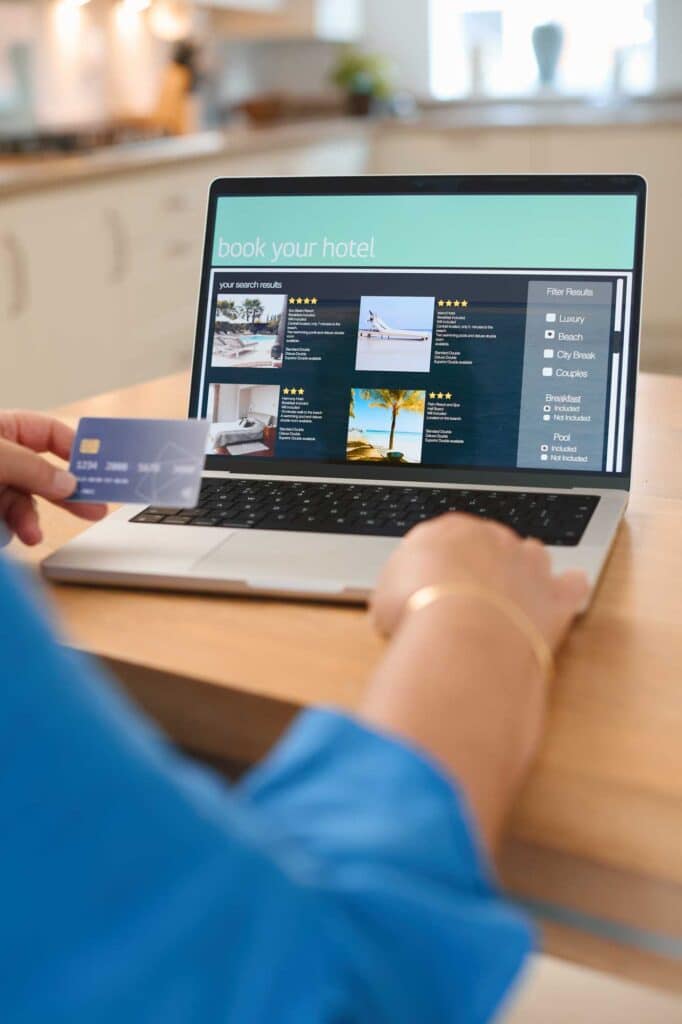 Eine Person, die mit einem Laptop und einer Kreditkarte in der Hand ein Hotel online bucht.