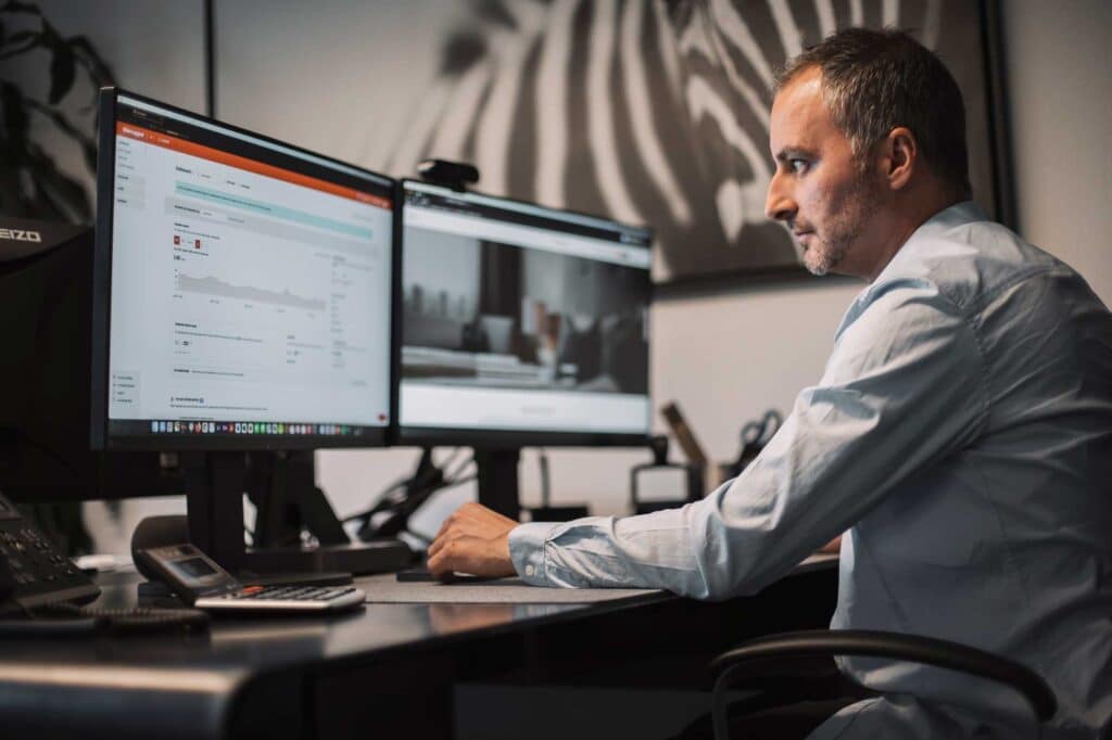 Ein Mann arbeitet an einem Schreibtisch mit zwei Monitoren in einem Full-Service-Büro der Werbeagentur.