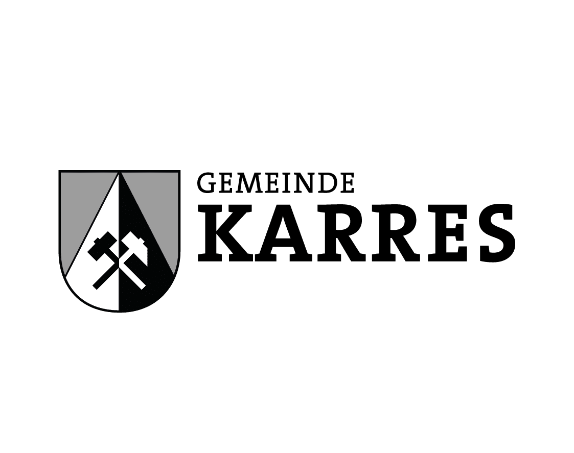 Schild mit zwei schwarzen Hämmern und Text GEMEINDE KARRES in fetten schwarzen Buchstaben.