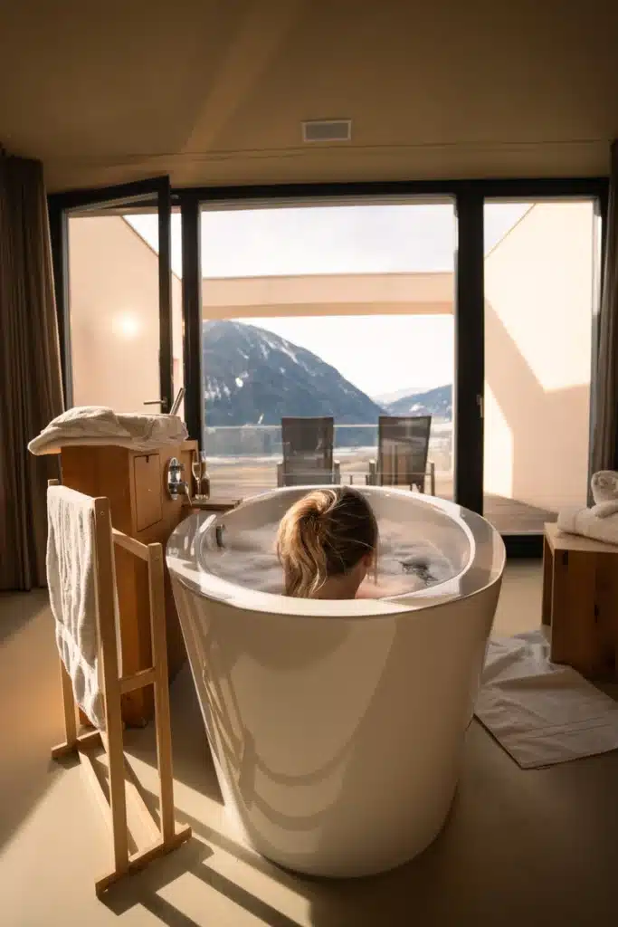 Eine Person entspannt sich in einer Badewanne im Referenz Hotel Bergwelt, Sonnenlicht und Bergblick am Fenster.